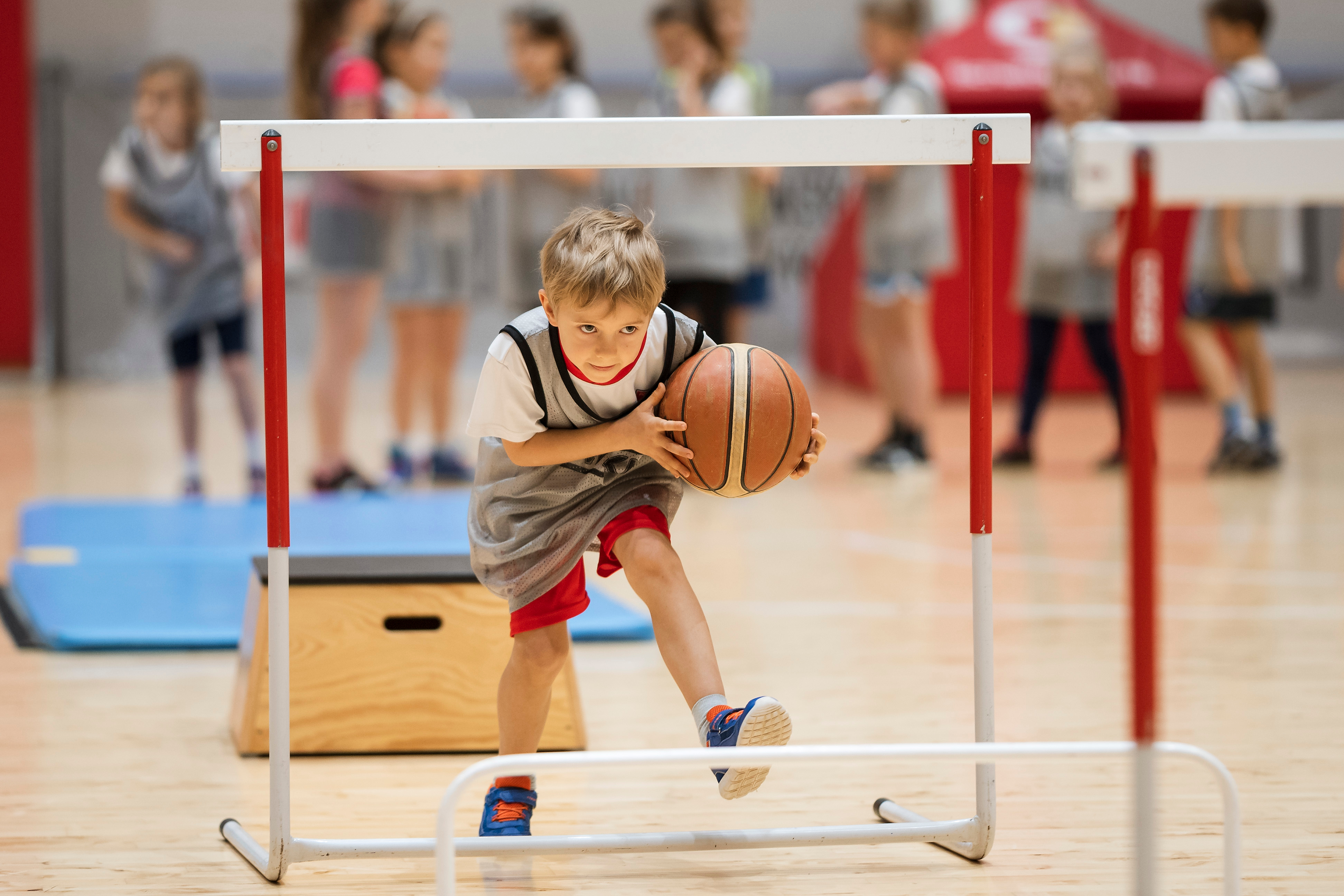 Een jongentje is met plezier aan het rennen met een basketbal onder een poortje door.